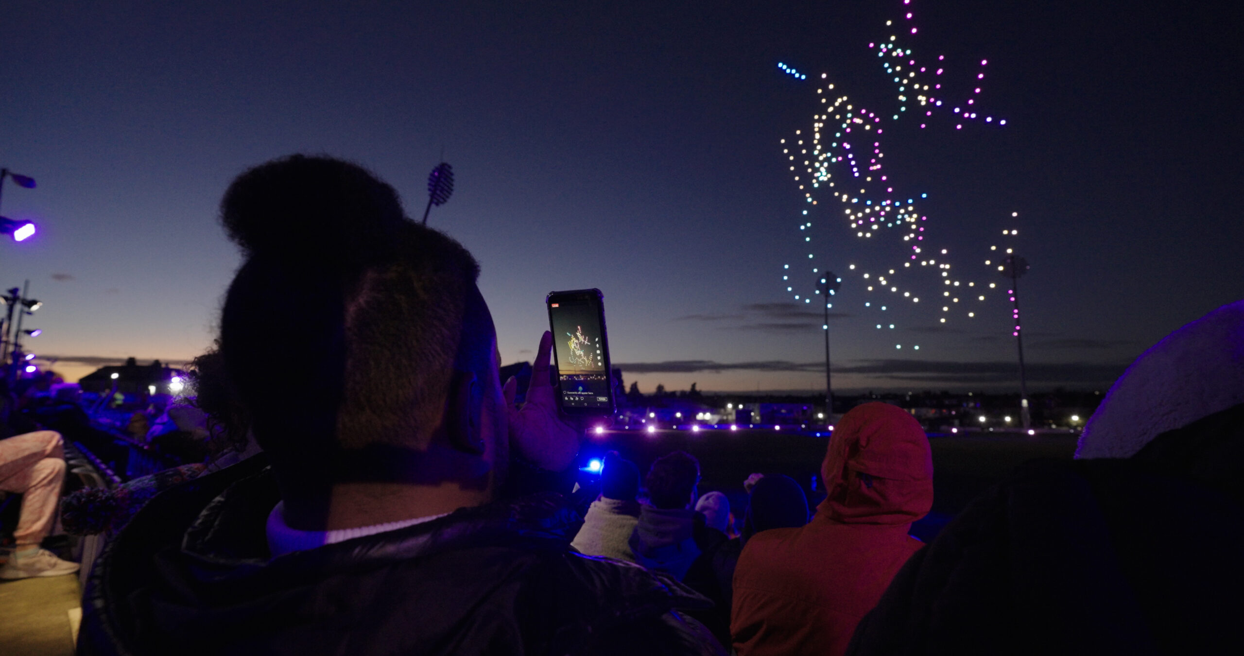 Guests watching and filming a colourful drone light show